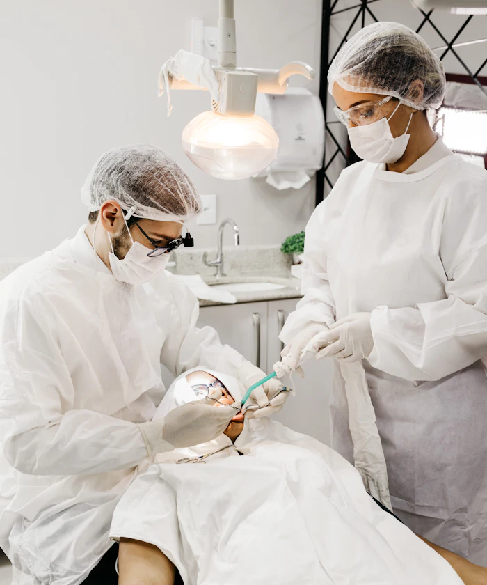 Two dentists in protective gowns treating a patient